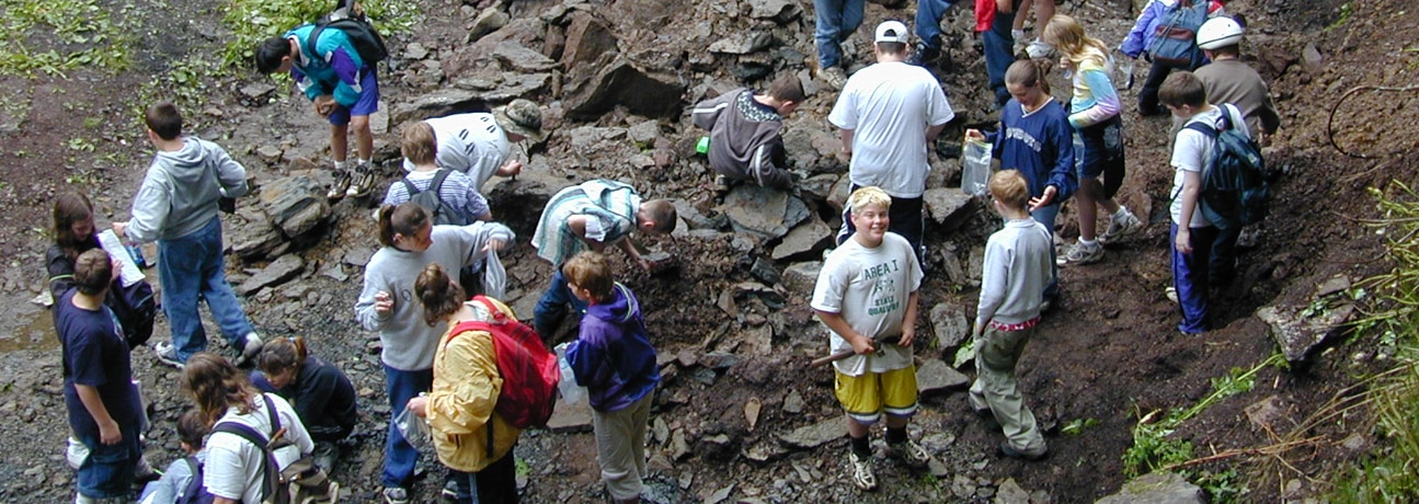 A group of students and workers explore through an area lined with various rocks.