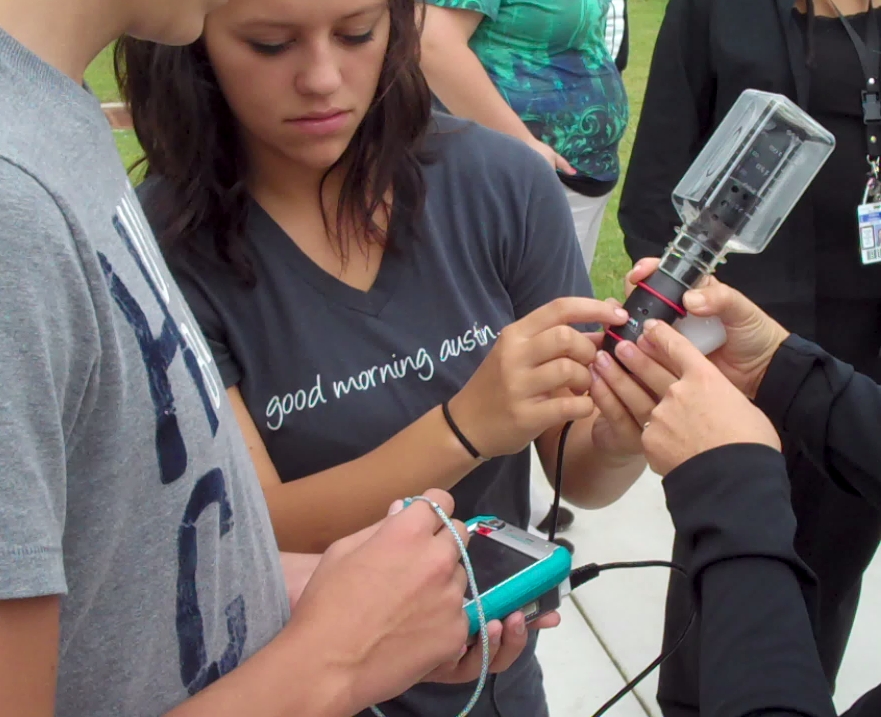 Two older children hold and examine a carbon dioxide meter during a learning activity.