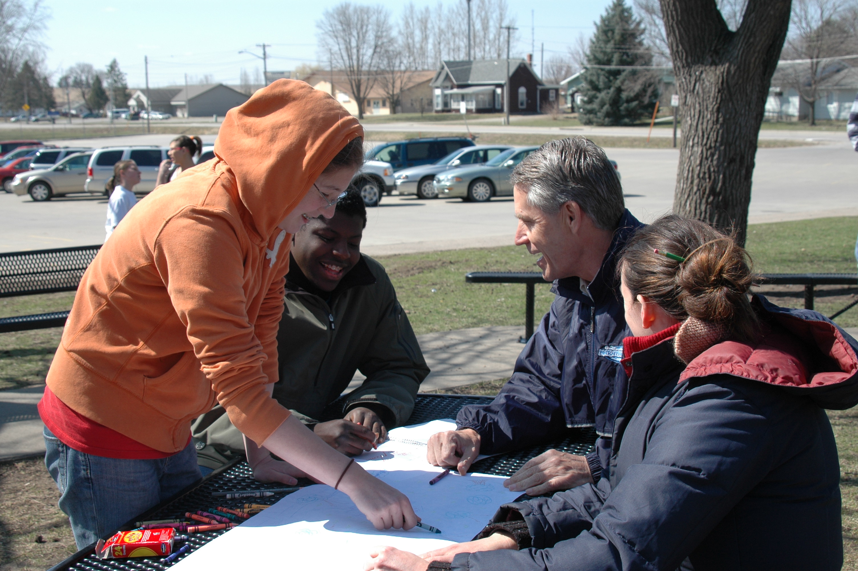 Three young adults and one teacher sit at a table outside during a learning activity.