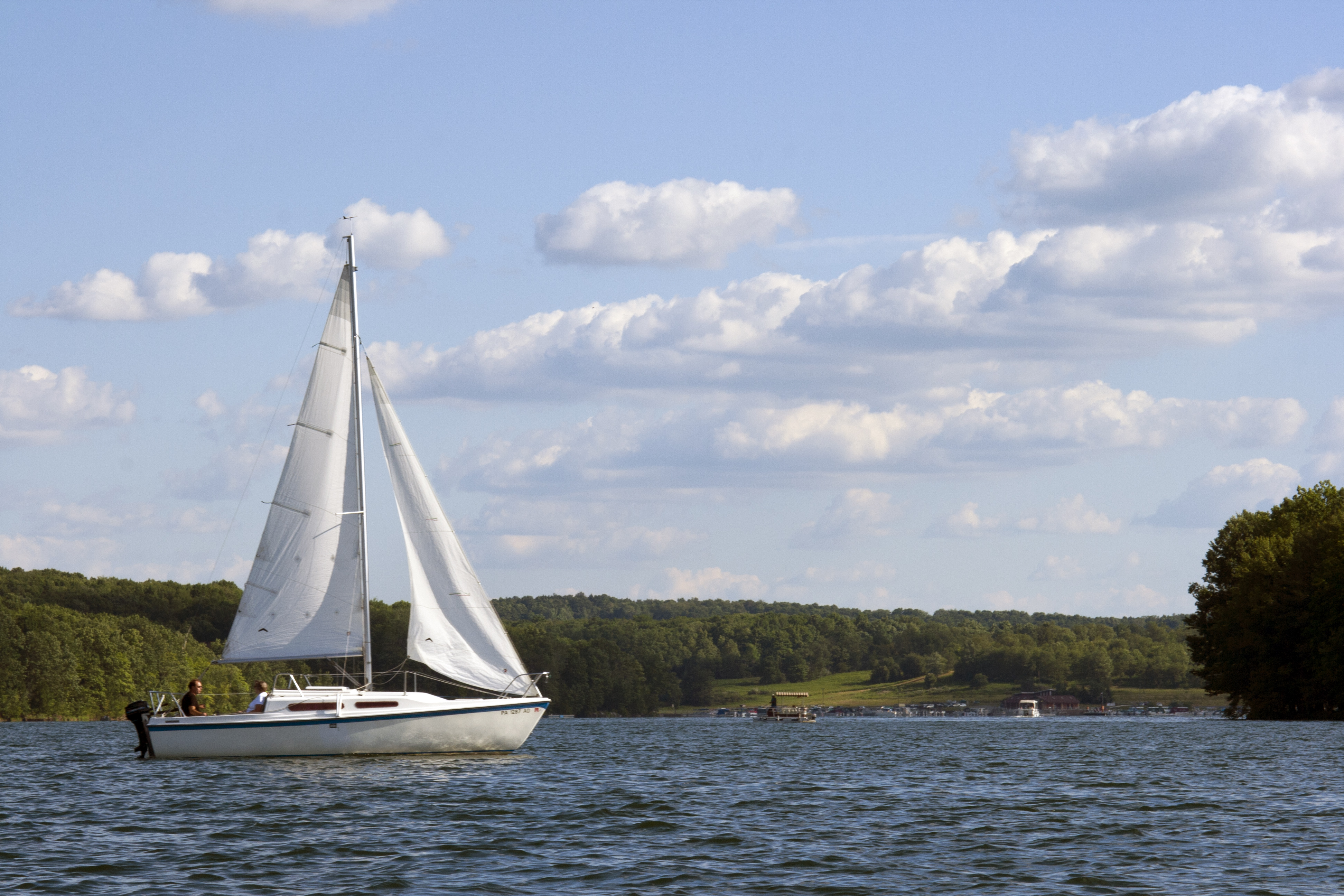 A white sailboat sailing on blue waters with mountains in the background