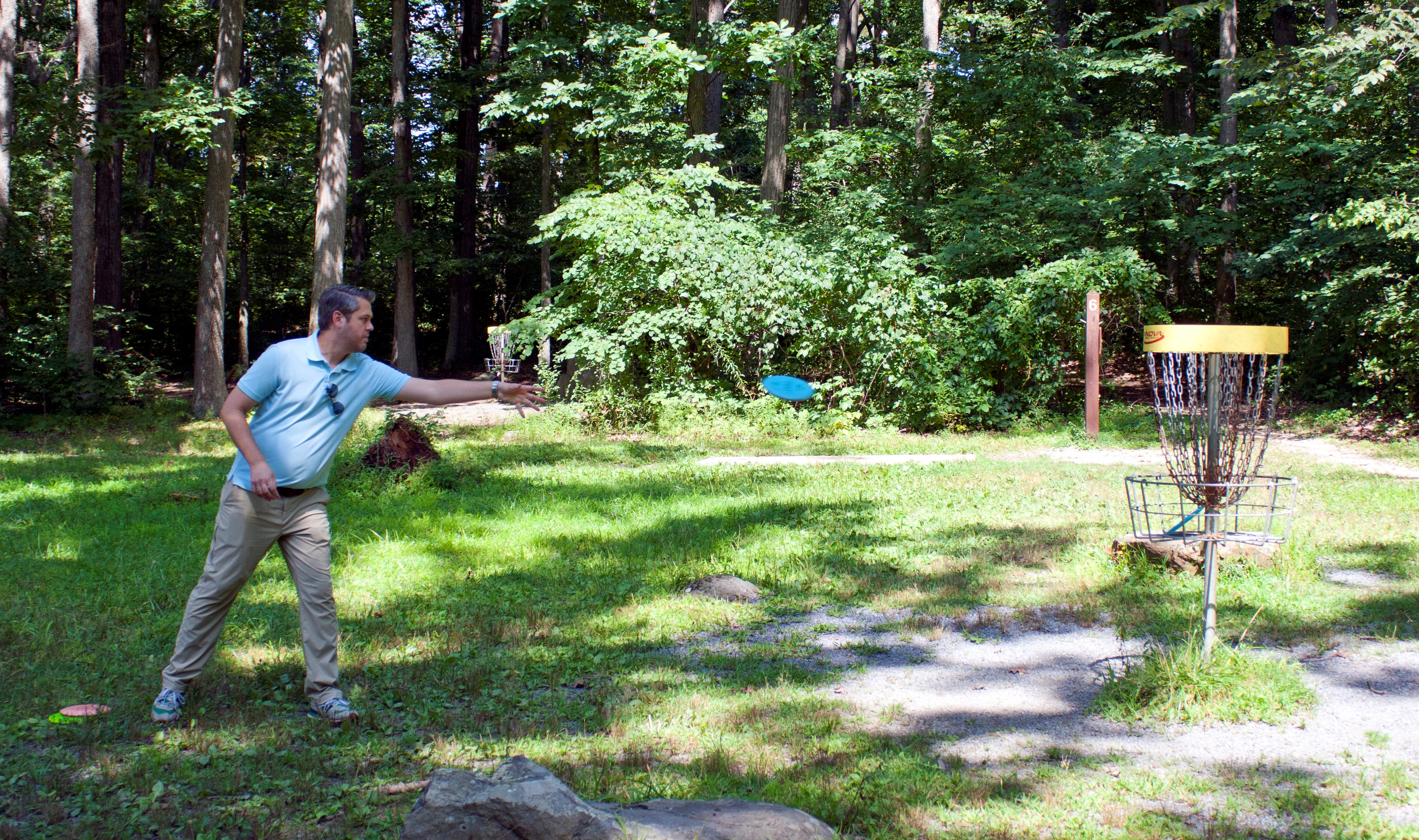 A man throwing a green disc at a yellow metal basket