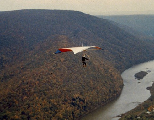 A man hangliding over a river in between mountains.