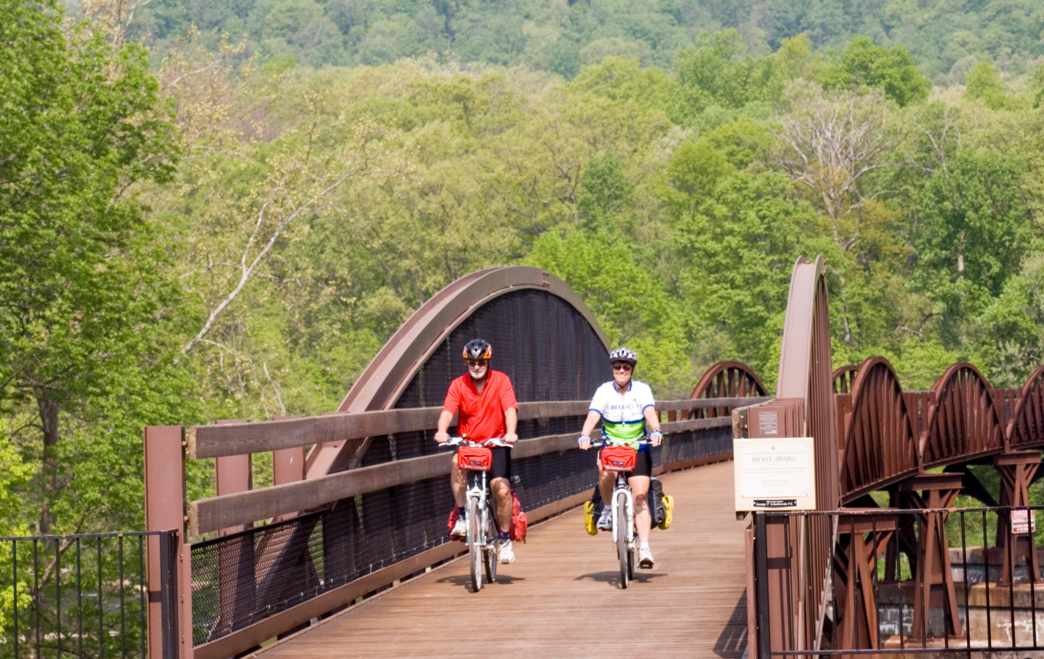 A man and a woman riding bicycles over a brown metal bridge