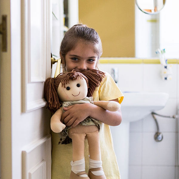 A smiling little girl standing in doorframe at home holding a doll.