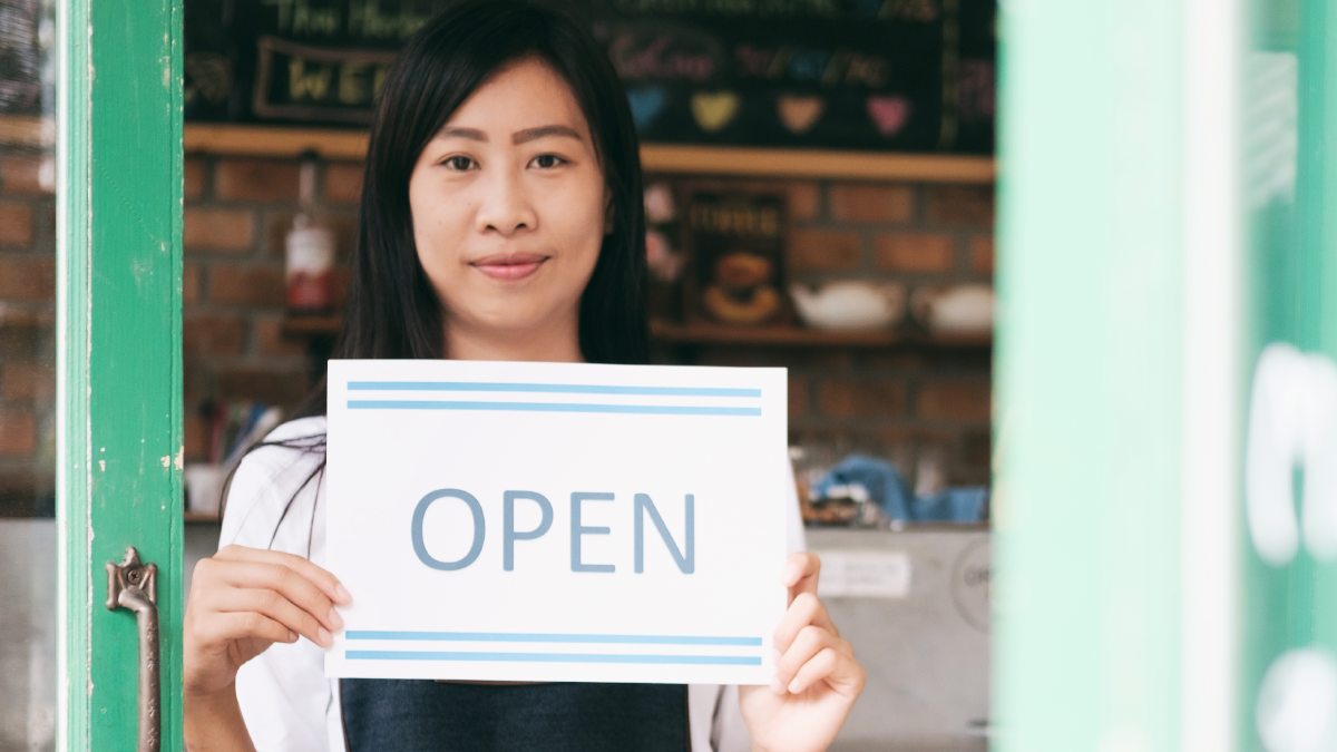Person holding an "Open" sign in front of a business