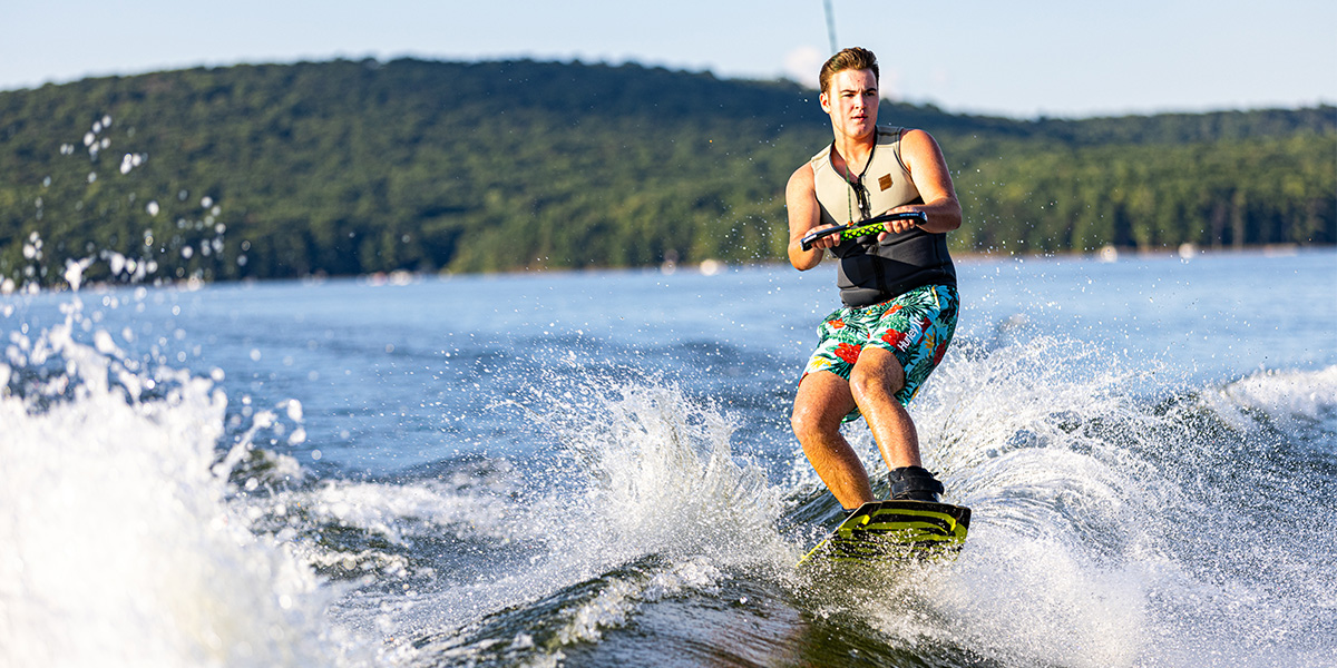 Photo Credit:  Scott Stover Photography. Young man wearing a life jacket and wake surfing while being towed by a boat.