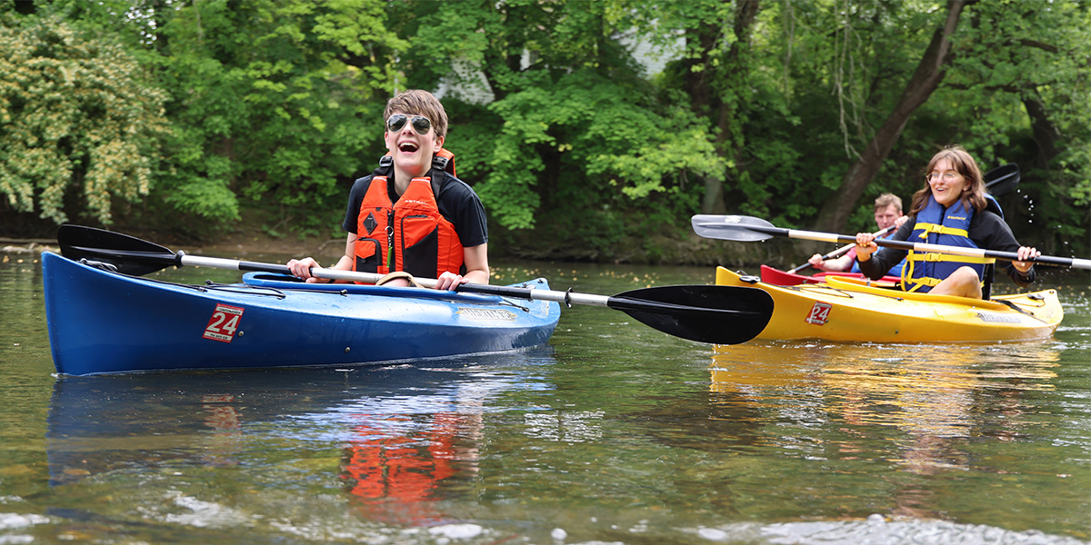 Three friends wearing life jackets are laughing and having fun while kayaking along a stream in Central Pennsylvania.