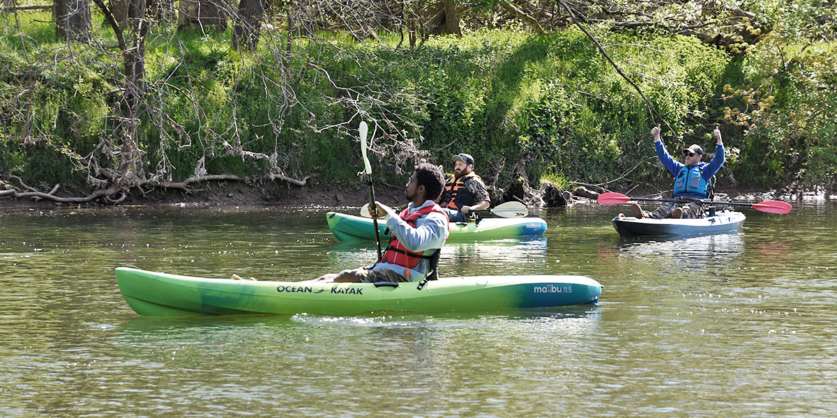 Three men wearing life jackets and kayaking on the Conestoga River