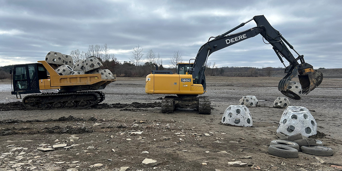 Excavators placing Concrete Reef Balls into the lake bottom of Woodcock Creek Lake for habitat improvement