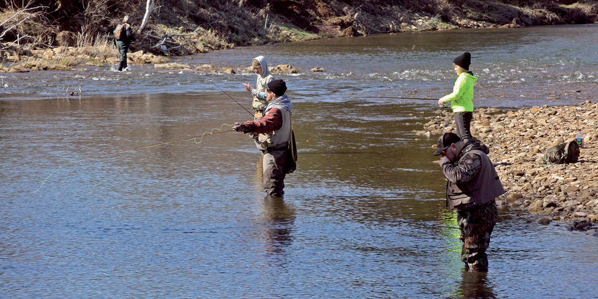 Two adults and two teenagers wade into a stream and fish along the shoreline of a public access stream in Northwest, Pennsylvania.