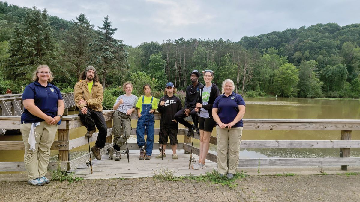 Group shot of two PFBC educators and a fishing class full of students by a lake 