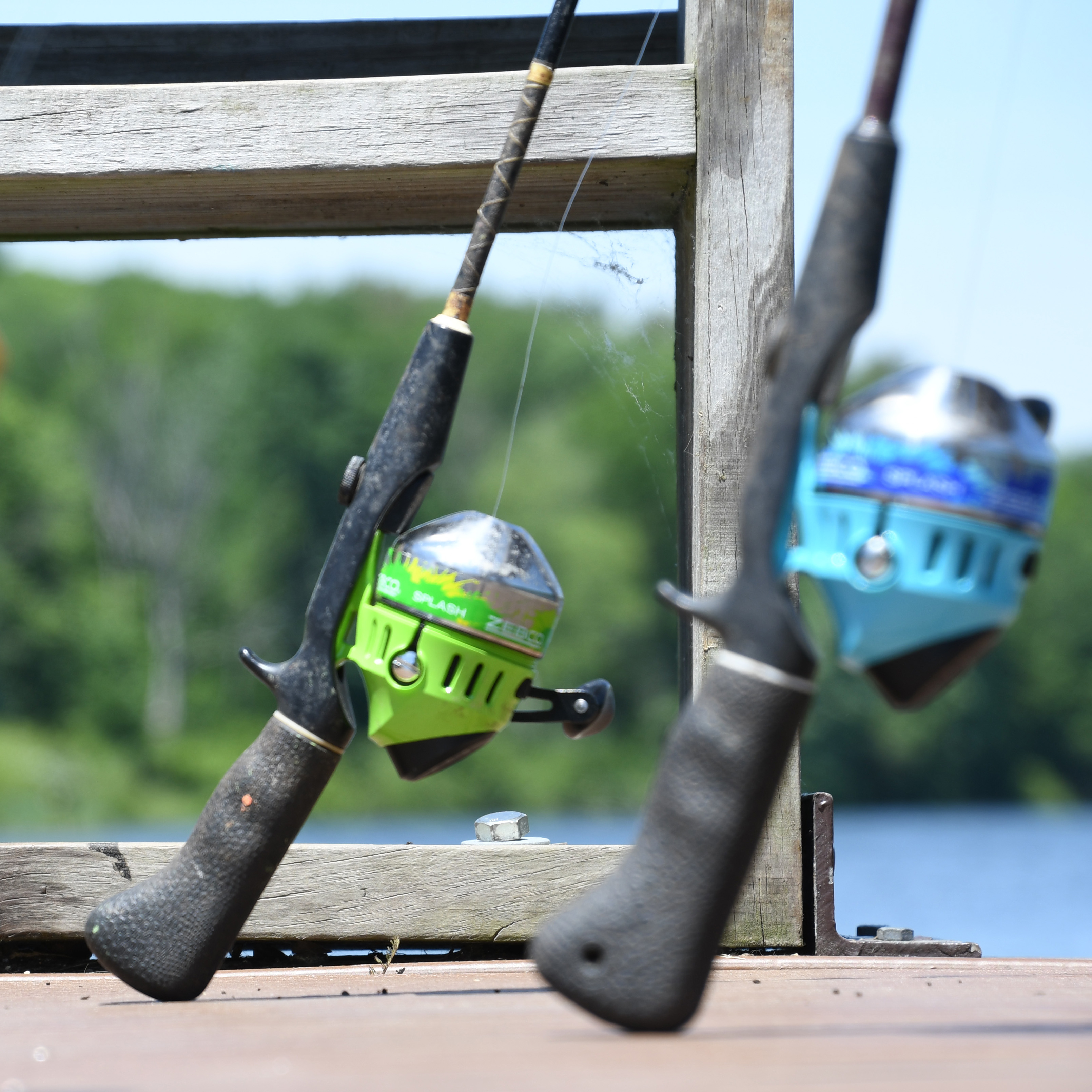 Close-up of two rods with closed-face reels leaning up against the railing of a wood dock.