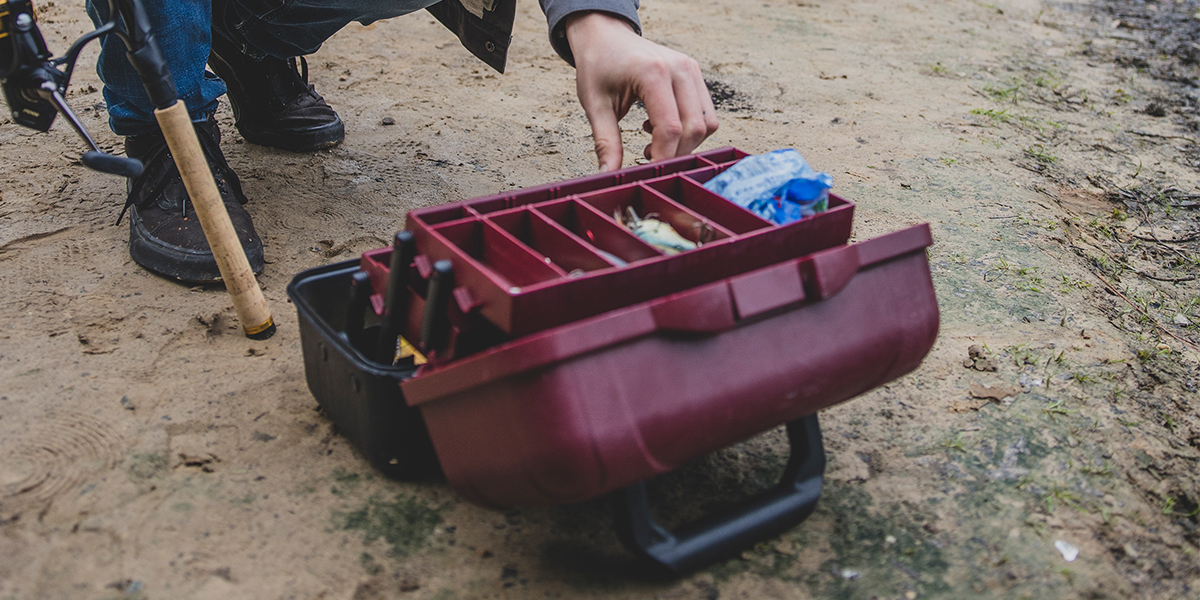 A close-up of a hand reaching into a tackle box to grab bait to hook onto a fishing rod.