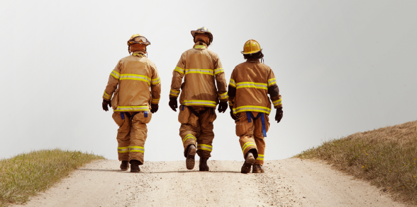 Three firefighters walk on a road together.