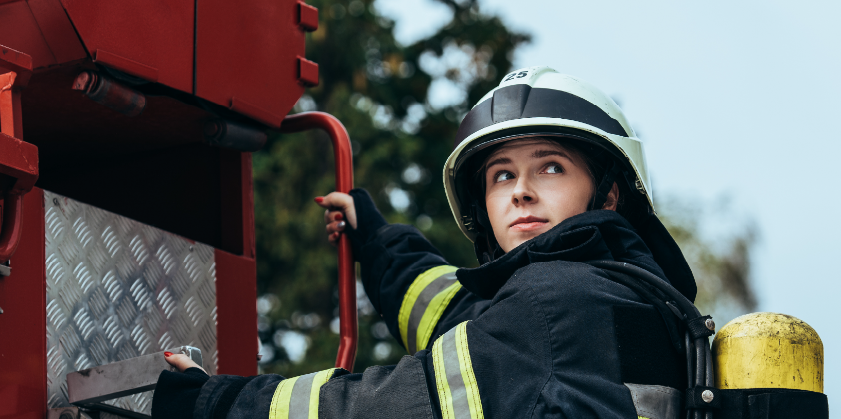 A firefighter climbs up on the back of a truck.