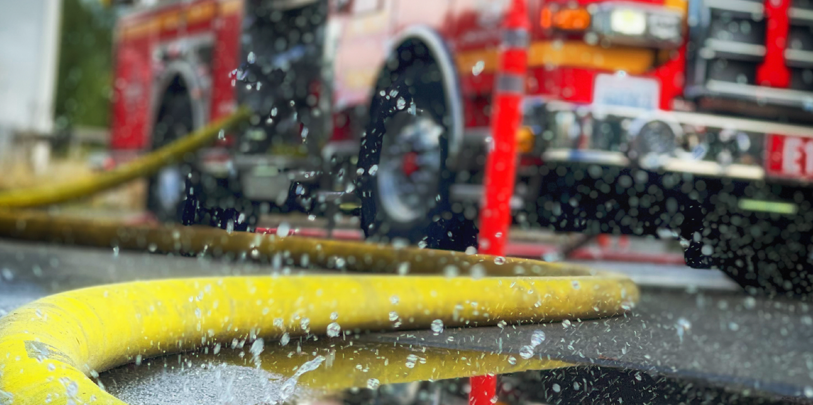 Close-up of a yellow hose on the ground in front of a firetruck.