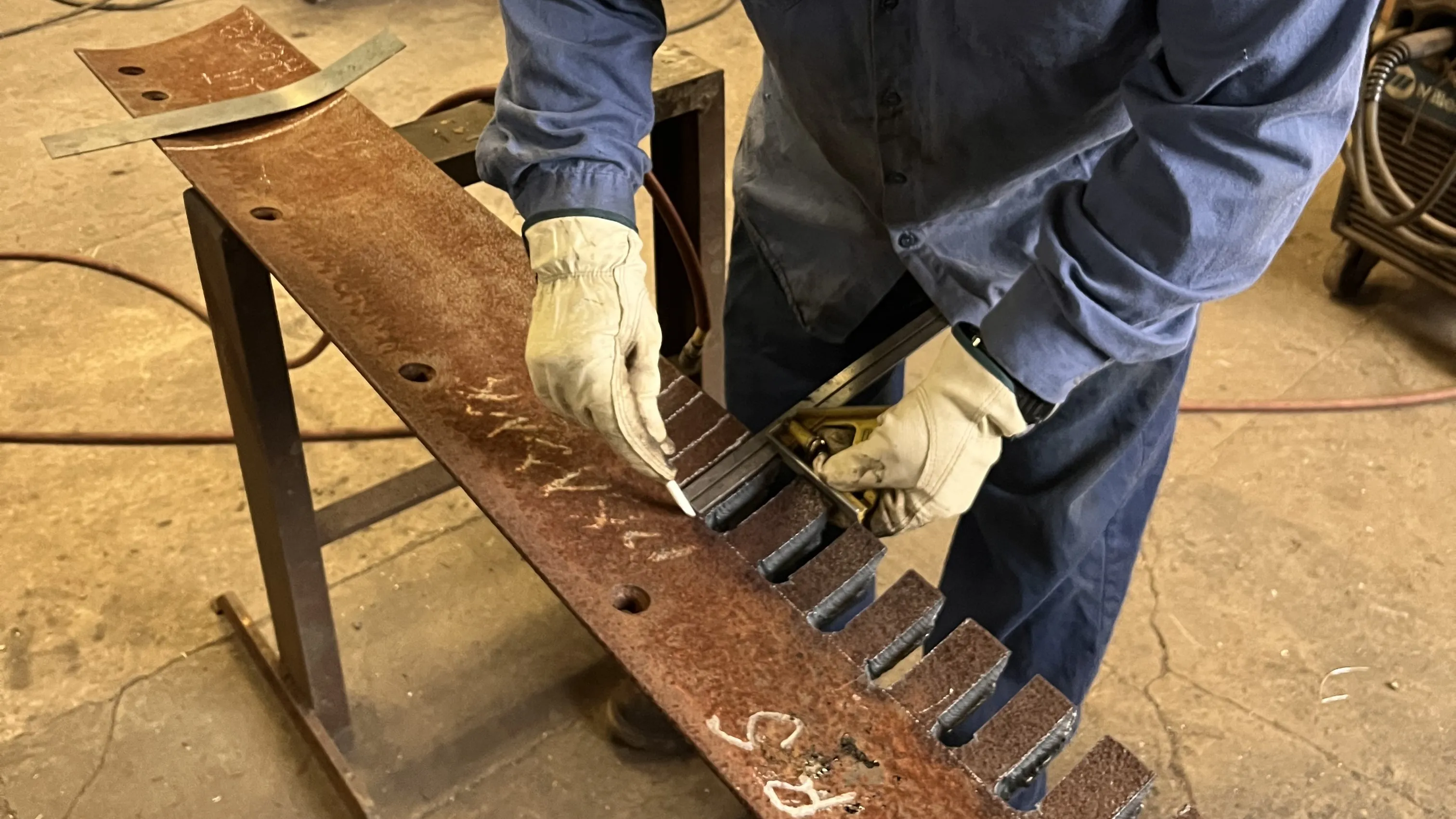 An image of a PennDOT employee wearing work gloves and marking a grader blade.