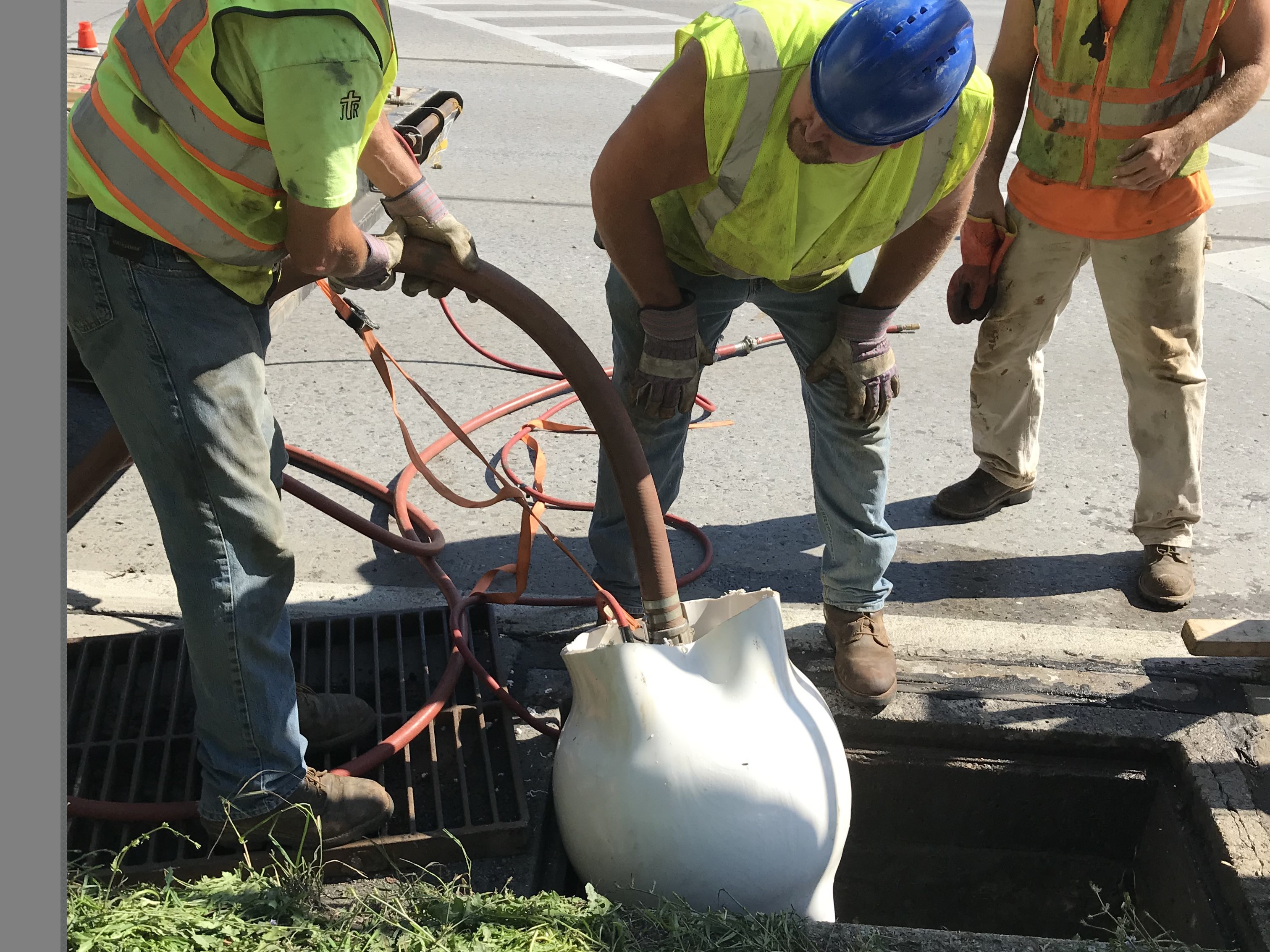 An image of three workers in hard hats and yellow safety vests applying steam to unfold the special white PVC liner