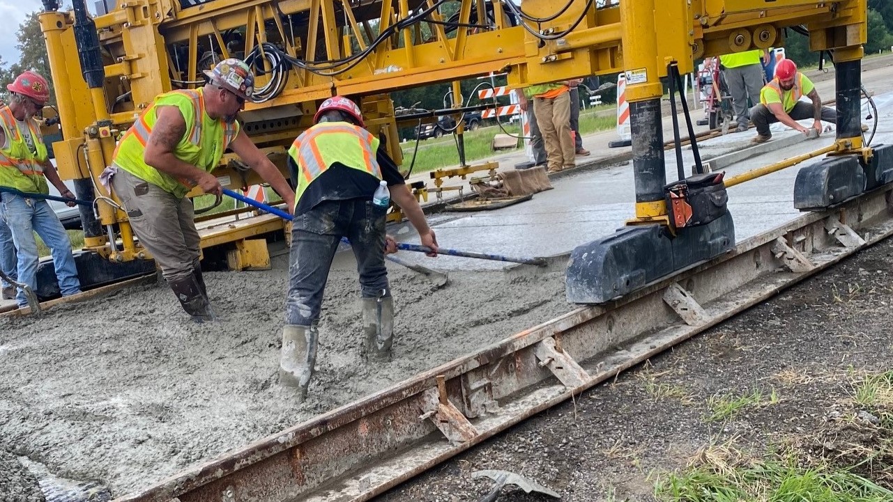 An image of construction workers in hard hats and yellow safety vests spreading concrete