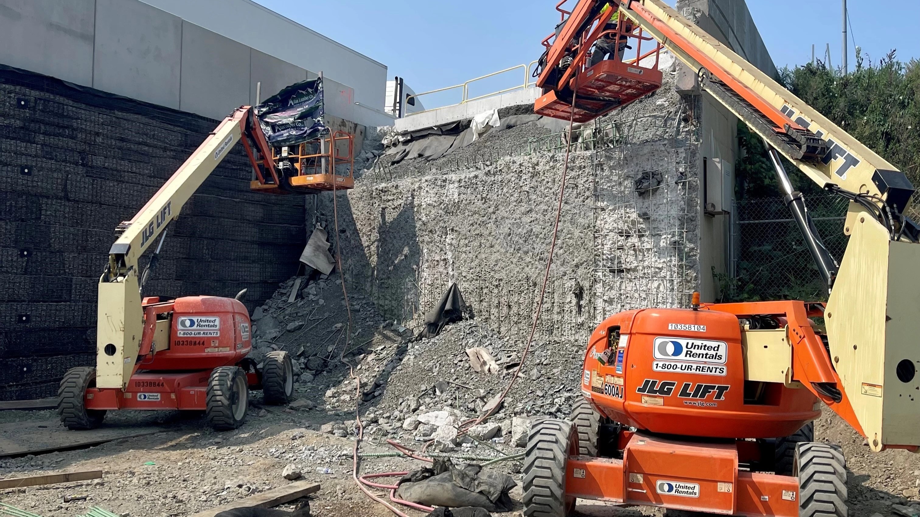 Drivable vertical mast lifts of being used to next to the temporary structure to continue clearing debris and preparing the worksite for reconstruction of the permanent structure to begin