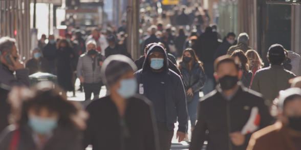 People wearing masks walk along a busy street.